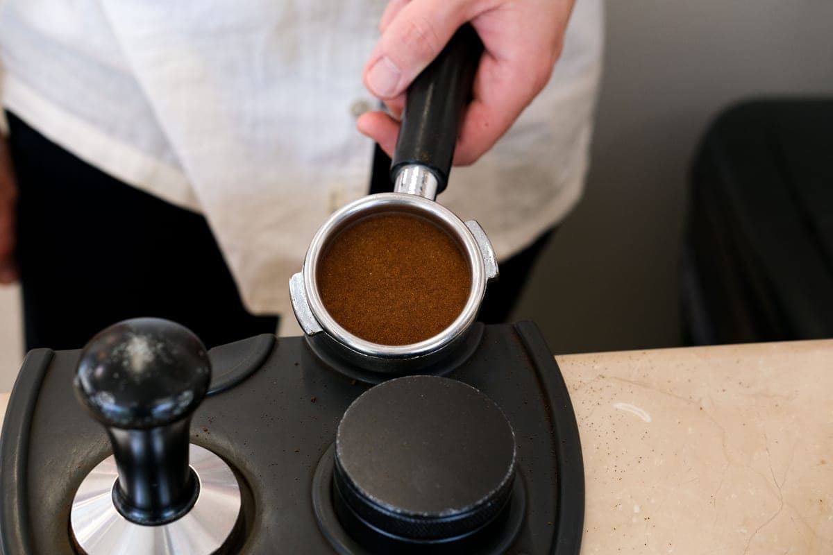 Fresh coffee grounds in a portafilter basket, ready to tamp, in warm light